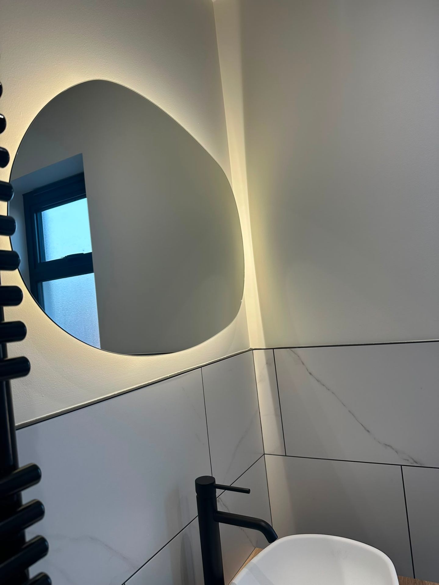 Backlit organic-shape LED mirror in a marble ensuite — feature bathroom lighting by D.P.L Electrical Services