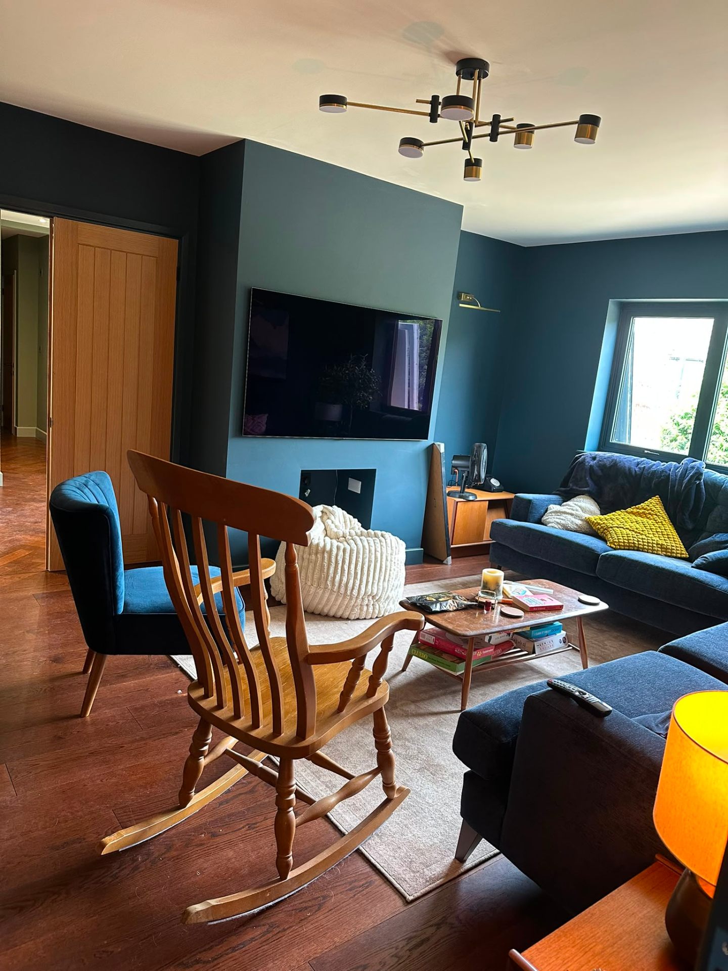 Teal living room with black-and-brass six-arm ceiling pendant and brass picture light above a wall-mounted TV — lounge lighting installation by D.P.L Electrical Services
