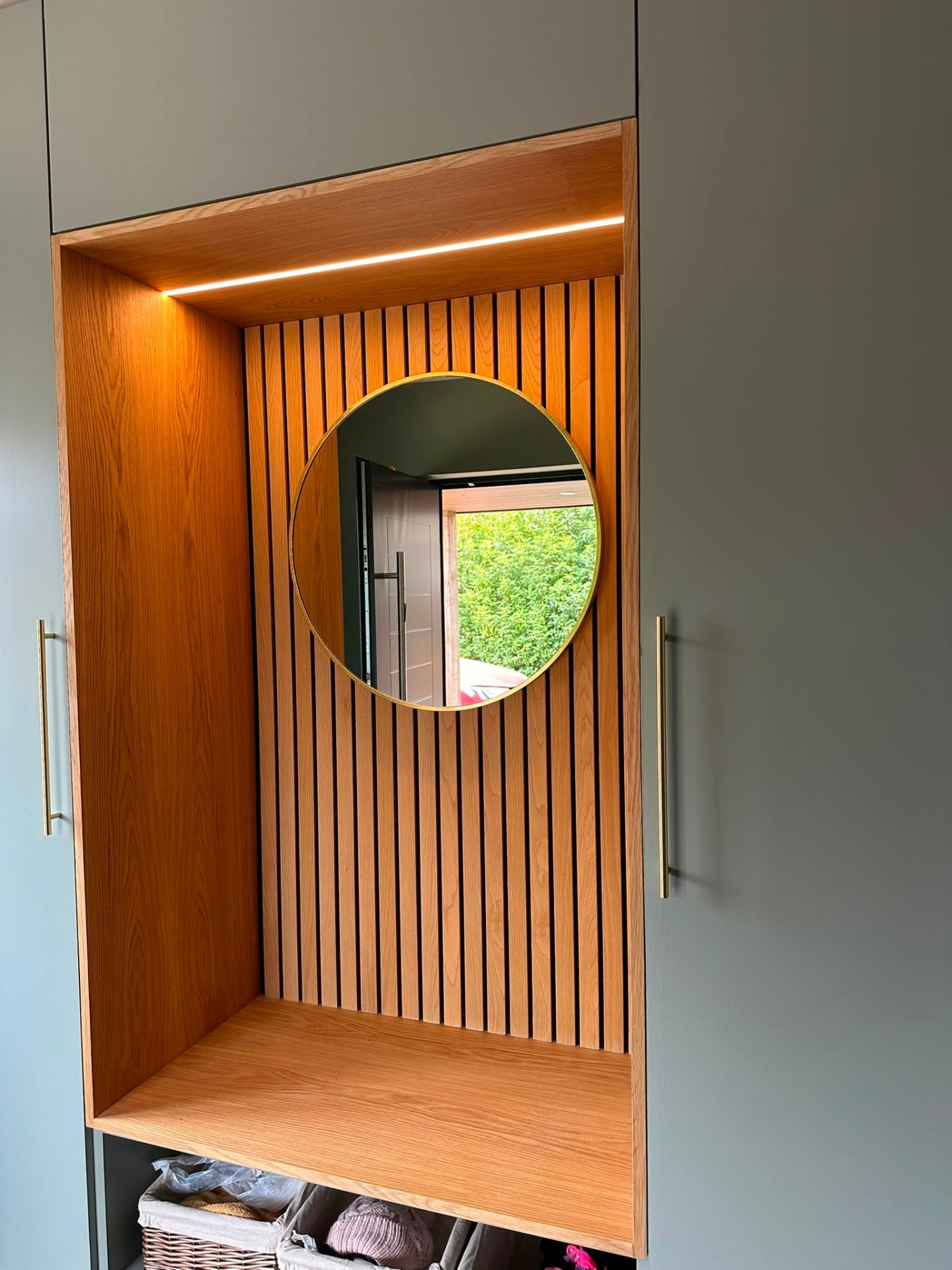 Bespoke oak slat joinery alcove with recessed warm LED strip above a round brass mirror — feature cabinet lighting installation by D.P.L Electrical Services