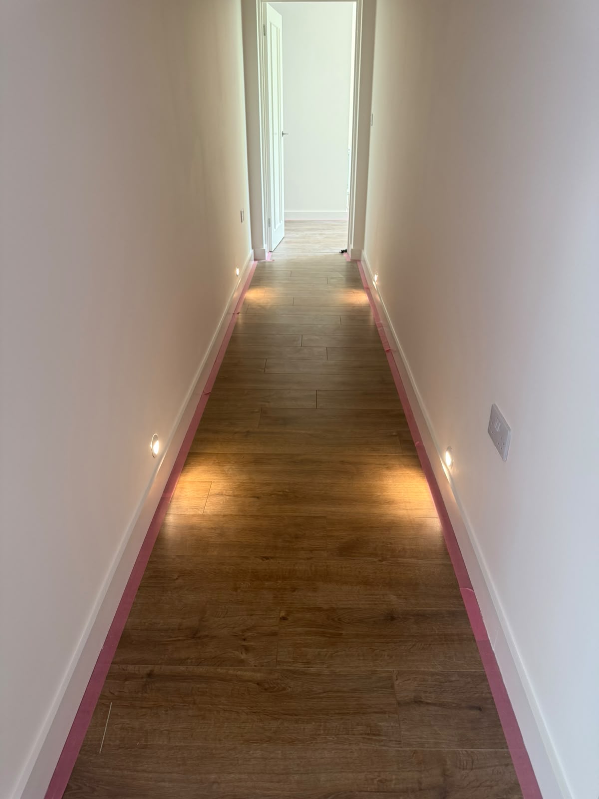 Hallway with recessed low-level LED wall lights casting warm pools onto oak flooring — bespoke lighting design by D.P.L Electrical Services
