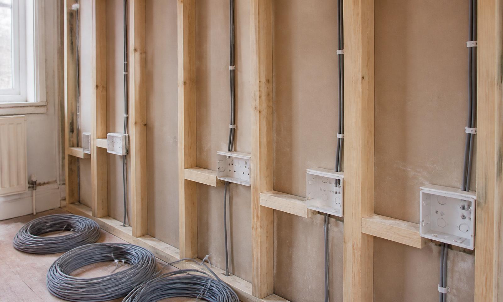 New twin-and-earth cables cleated through timber studs into fresh white back boxes with coils of unused cable on the floor — full domestic rewire in progress by D.P.L Electrical Services